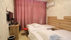 Een hotelkamer met twee bedden, een bureau met stoel, een prullenbak en een airconditioning.