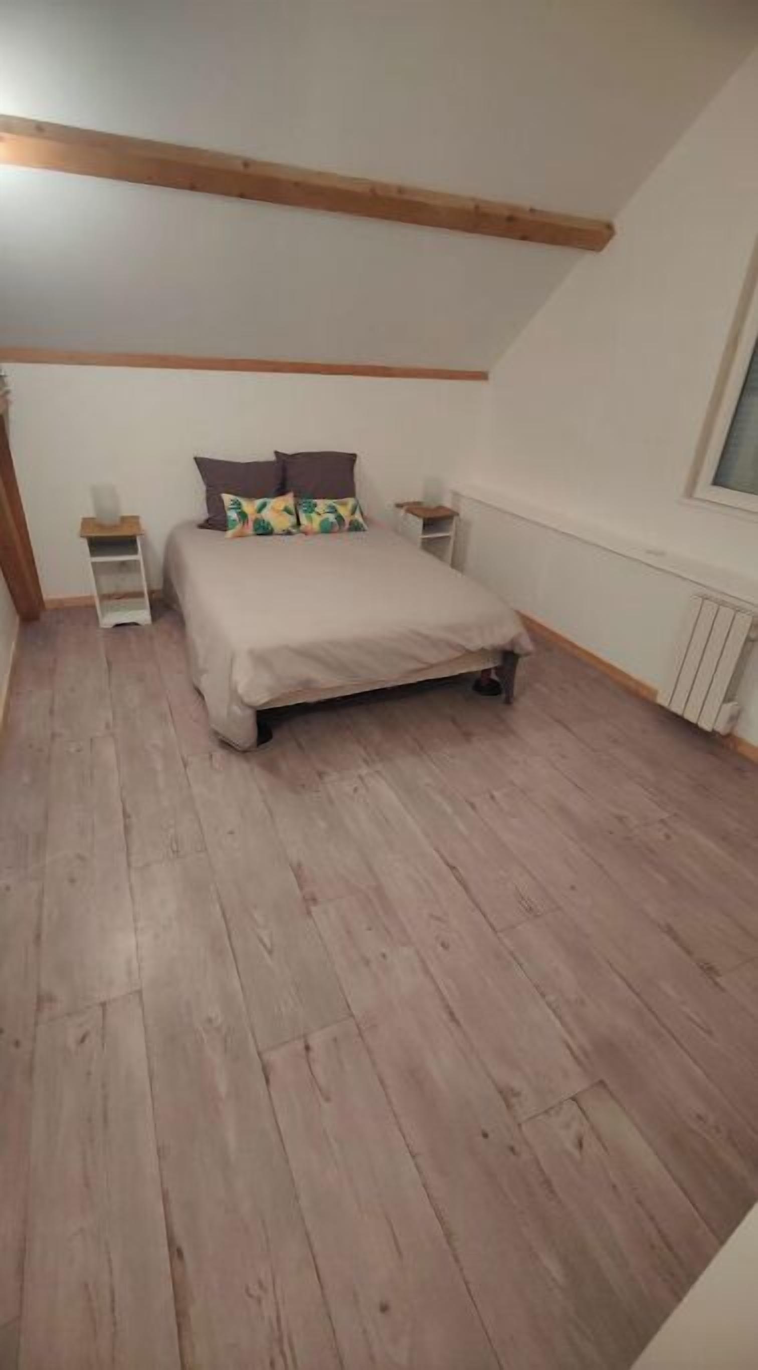 A bedroom with a wooden floor, a bed with a beige cover, two nightstands, and a window.
