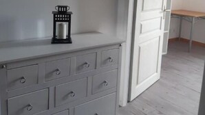 A room with a white dresser, a framed picture on the wall, and a door leading to another room.
