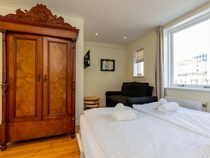 A hotel room with a large wooden wardrobe, a black sofa, a bed with white linens, and a window with a city view. - Apartment in Vlissingen Near the Beach (Vlissingen)
