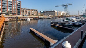 A marina with boats docked, a wooden pier, and a modern building with a crane in the background. - Apartment in Vlissingen Near the Beach (Vlissingen)
