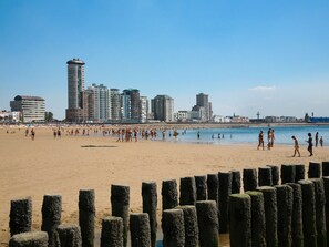 A beach with a city skyline in the background, wooden posts in the foreground, and people enjoying the beach. - Apartment in Vlissingen Near the Beach (Vlissingen)