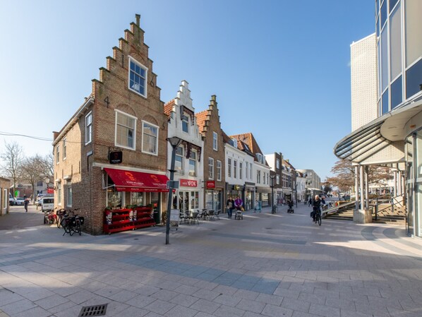 Una calle con arquitectura europea tradicional, que incluye una tienda con toldo rojo y un edificio moderno con grandes ventanales.