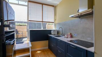 A compact kitchen with dark cabinets, a white countertop, a built-in oven, and a window with blinds.
