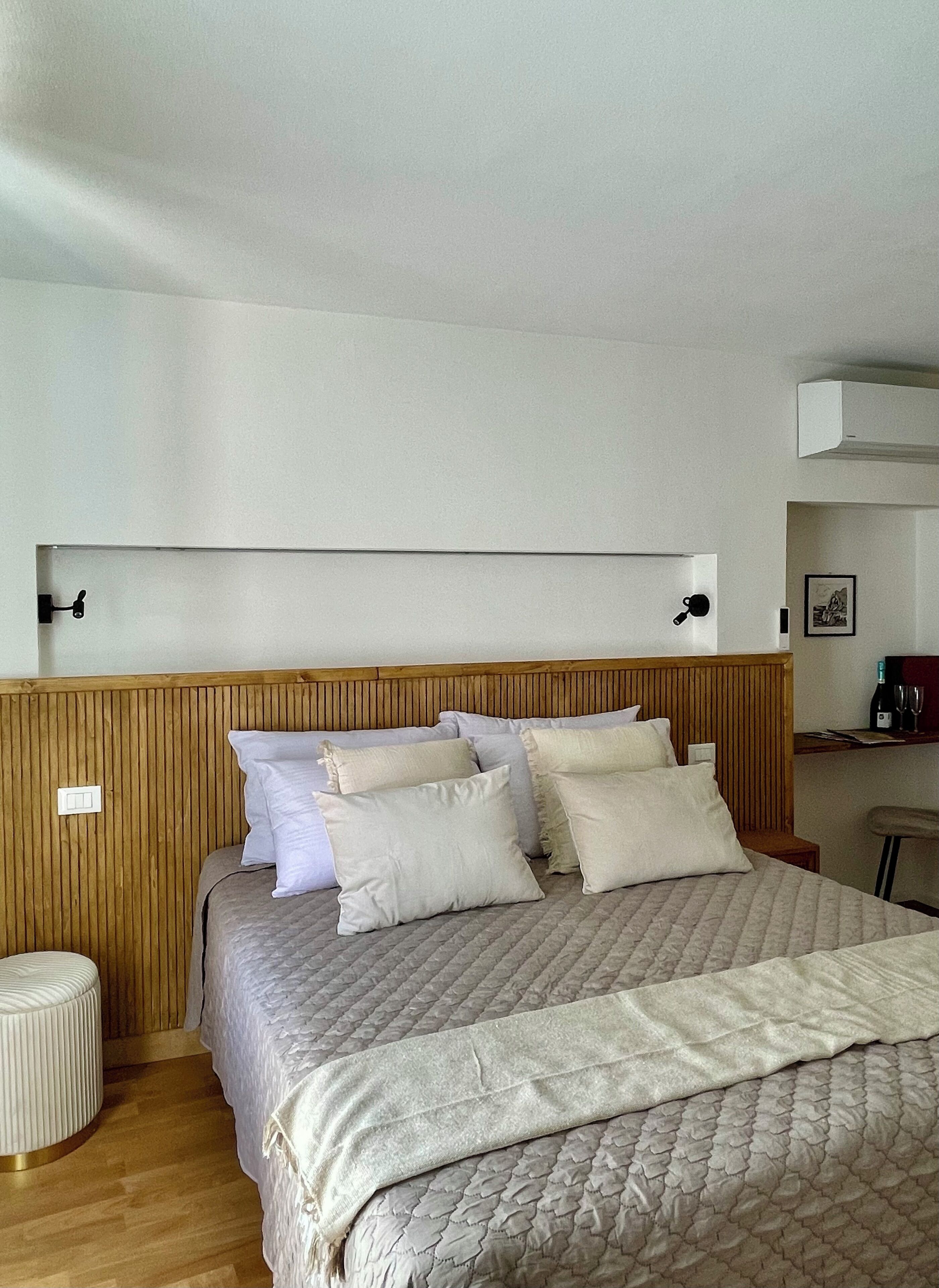 A bedroom with a wooden headboard, a bed with a quilted cover, and a bedside table with a wine bottle and glasses.