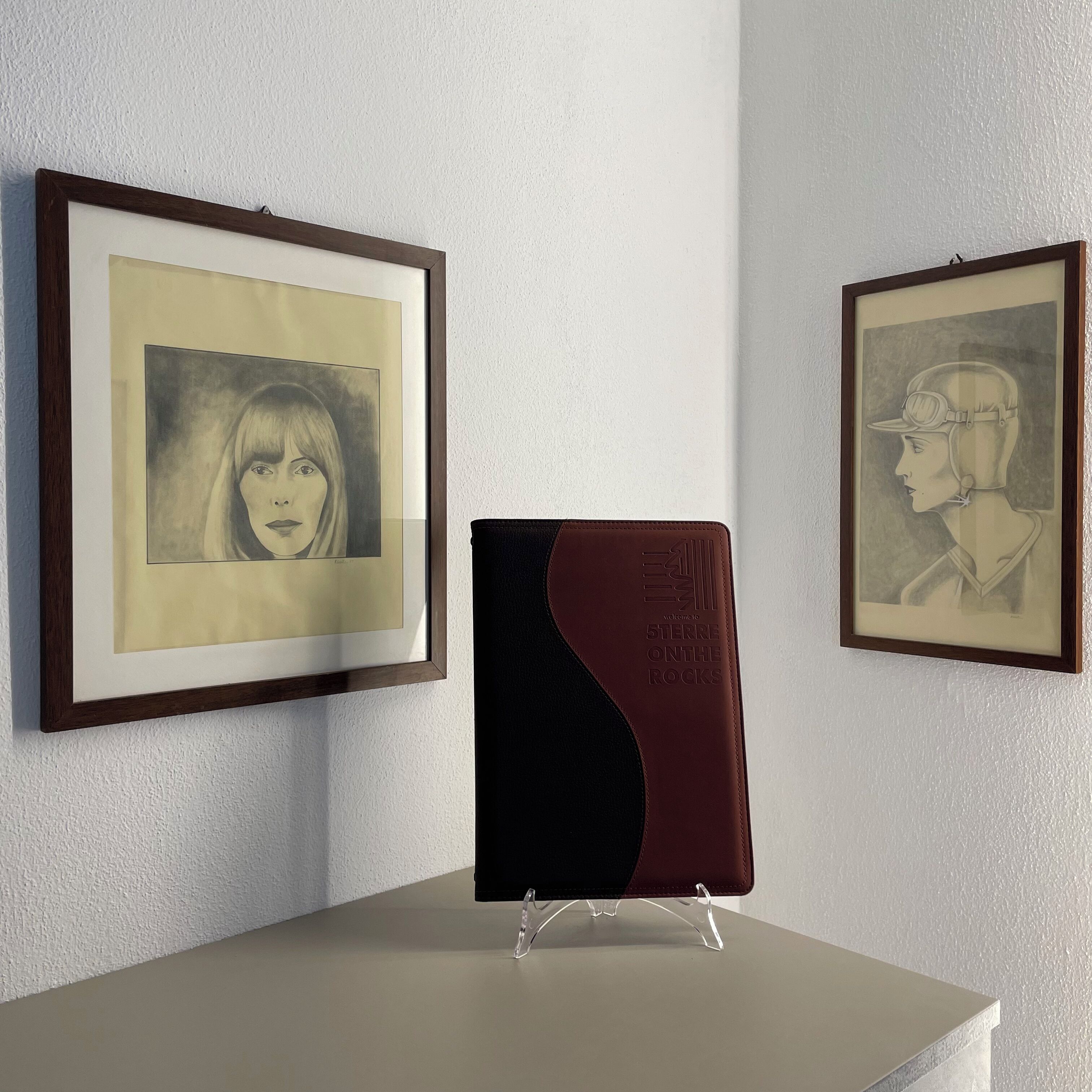 A framed artwork on a wall, a book on a stand, and another framed artwork.
