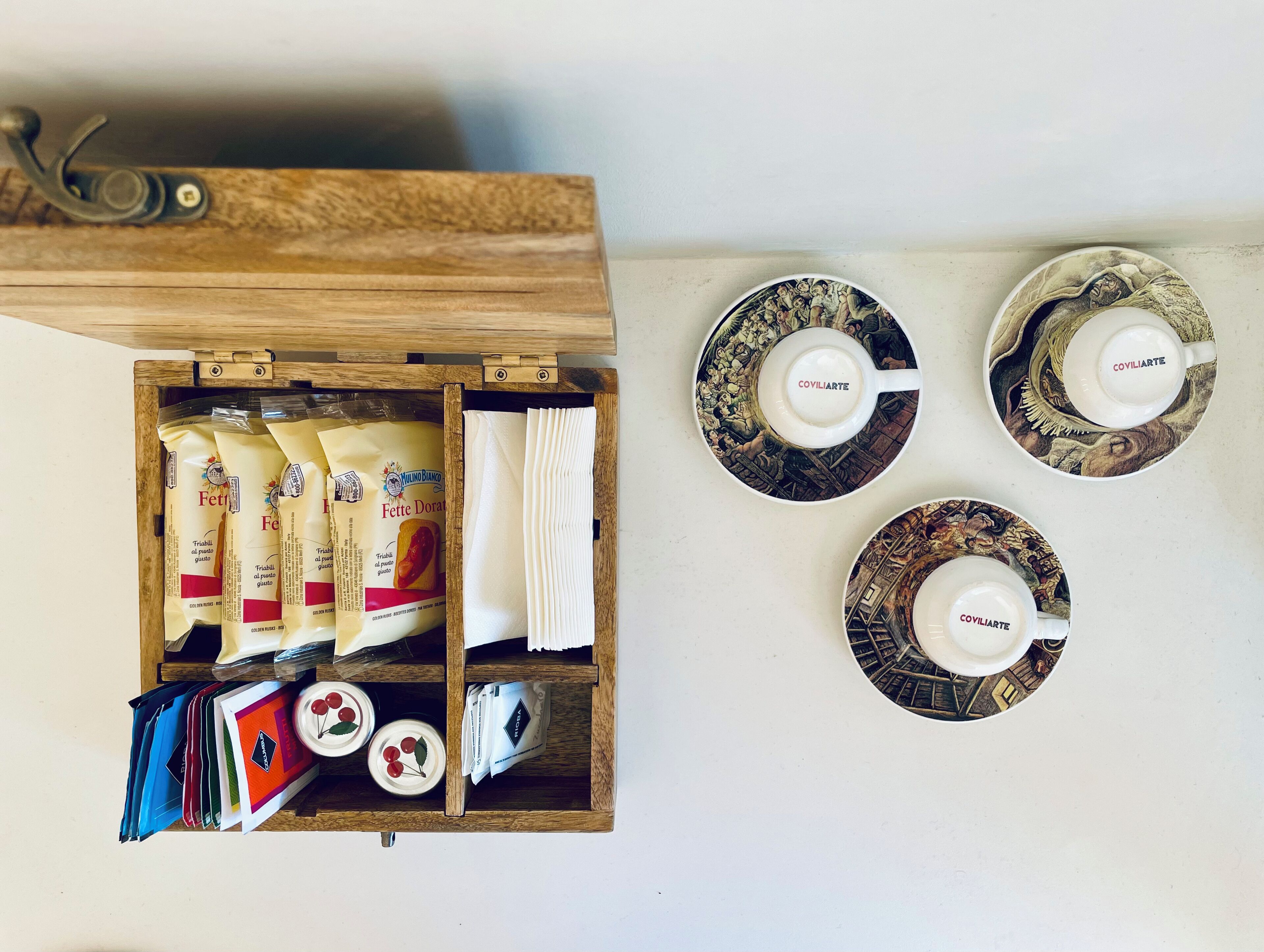 A wooden drawer with pasta packets and a white napkin. On the wall, there are three plates with 'COVILIARTE' and a cup, and a wooden shelf with colorful folders.