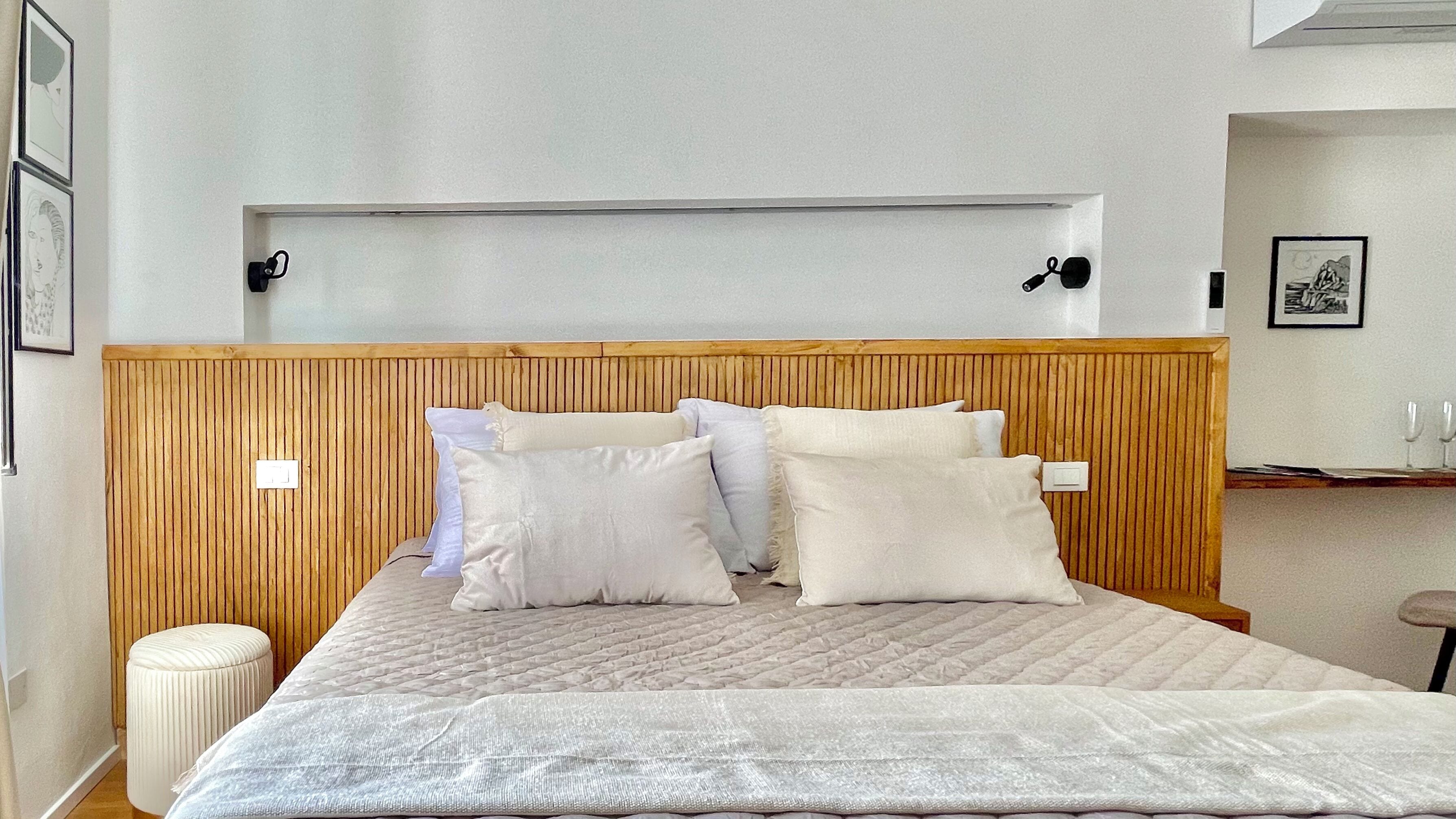 A bedroom with a wooden headboard, a bed with white bedding, and a small bedside table with two glasses.