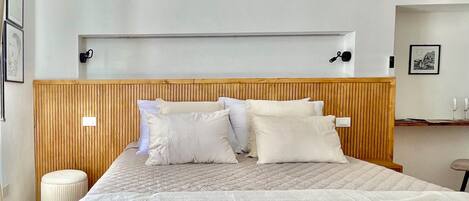 A bedroom with a wooden headboard, a bed with white bedding, and a small bedside table with two glasses.