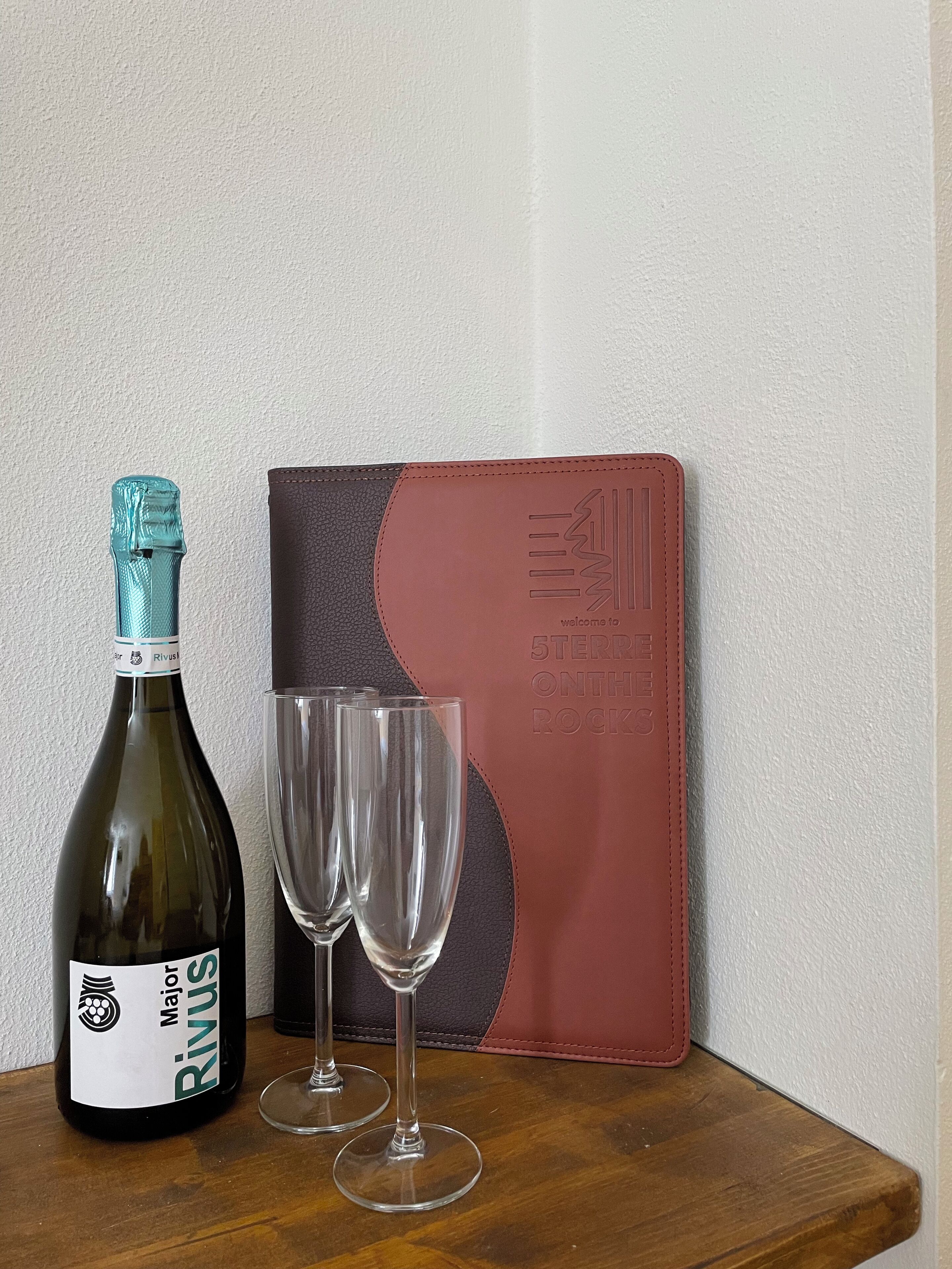 A bottle of Major Rivus wine, two empty wine glasses, and a leather-bound notebook with embossed text.