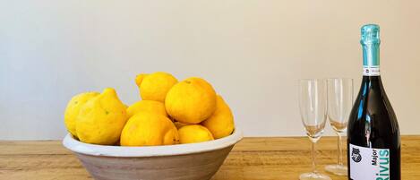 Un cuenco de limones, una botella de RIVUS vino y dos copas sobre una mesa de madera frente a una pared blanca con tres cuadros enmarcados.