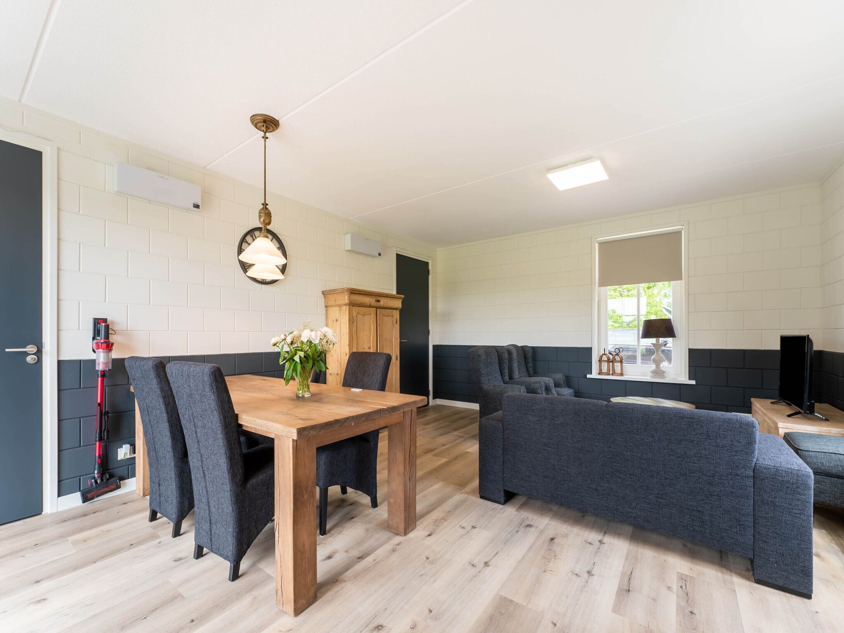 En moderne stue med et træspisebord, grå polstrede sofaer og en mørk væg.