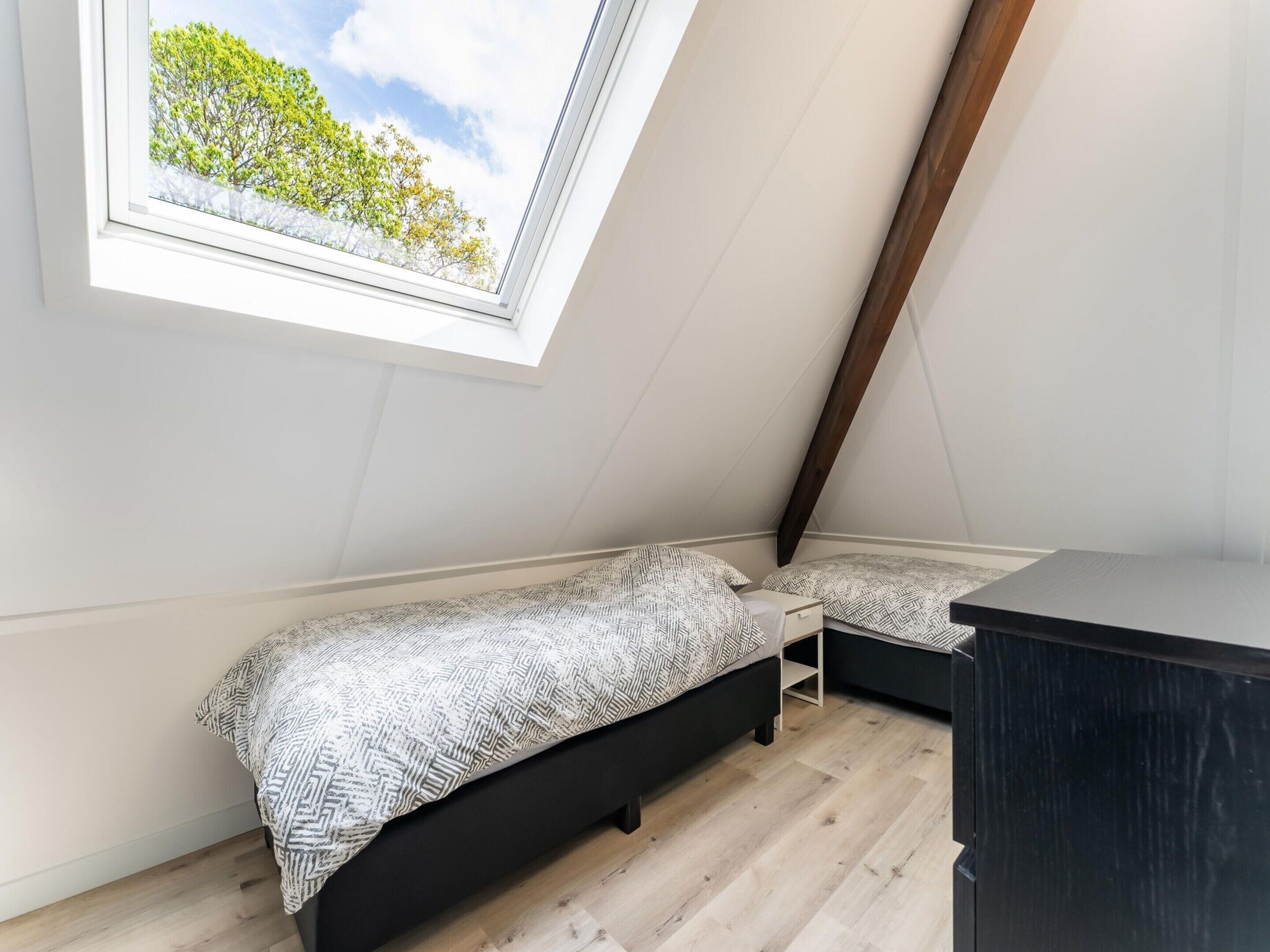 A small, modern bedroom with a sloped ceiling and a skylight, featuring a bed and a dresser.