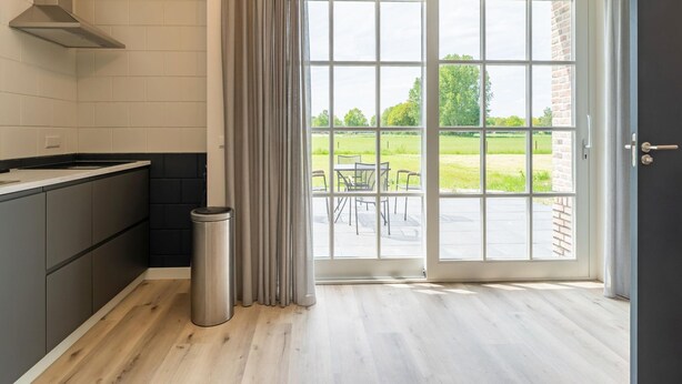 Une cuisine moderne dotée d’une grande fenêtre, offrant une vue sur un paysage verdoyant, et d’une porte donnant sur un espace extérieur.