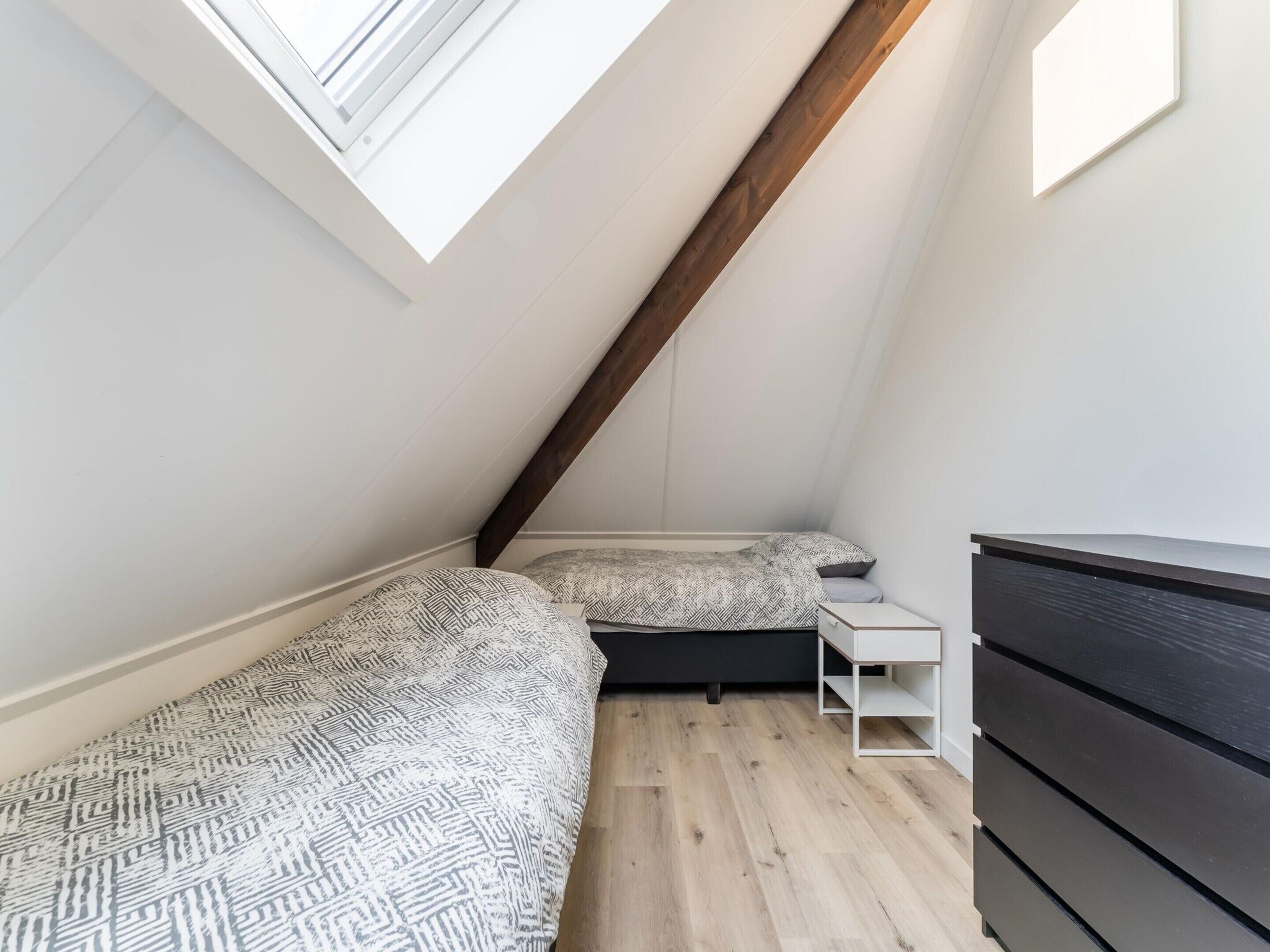 Et lille værelse med skråt loft, to senge, en kommode og et ovenlys.
