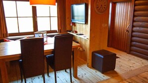 A wooden cabin interior with a dining table, chairs, a television, and a clock on the wall. - Wastl Comfortable Holiday Residence (Woergl)