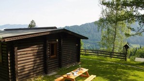 A wooden cabin with a picnic table in a grassy area, surrounded by trees and mountains. - Wastl Comfortable Holiday Residence (Woergl)