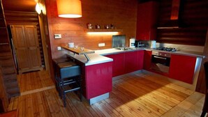 A modern kitchen with wooden flooring, a central island, red cabinetry, and a built-in oven. - Wastl Comfortable Holiday Residence (Woergl)