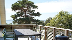 A wooden deck with a table and chairs, a barbecue grill, and a view of trees and water. - 4 Star Holiday Home in Stromstad (Stromstad)