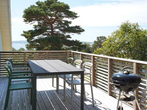 Un terrazzo in legno con tavolo e sedie, un barbecue e vista su alberi e acqua.