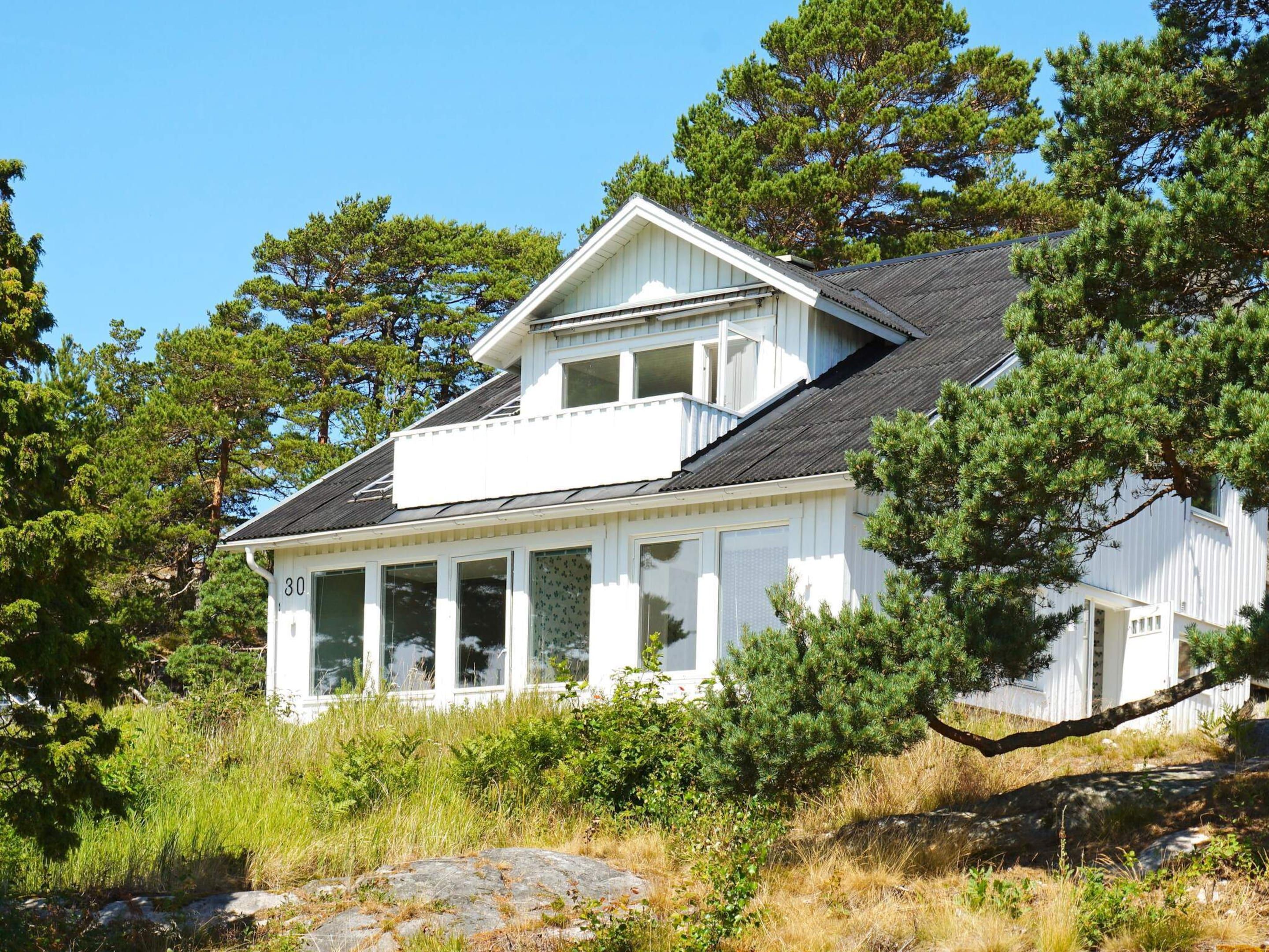 A white house with a covered porch, surrounded by trees and natural landscape.