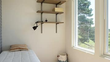 Un dormitorio con cama, ventana con vista a árboles y estante con lámpara.