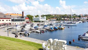 Uma marina com barcos atracados, uma grande escultura branca e edifícios ao fundo.