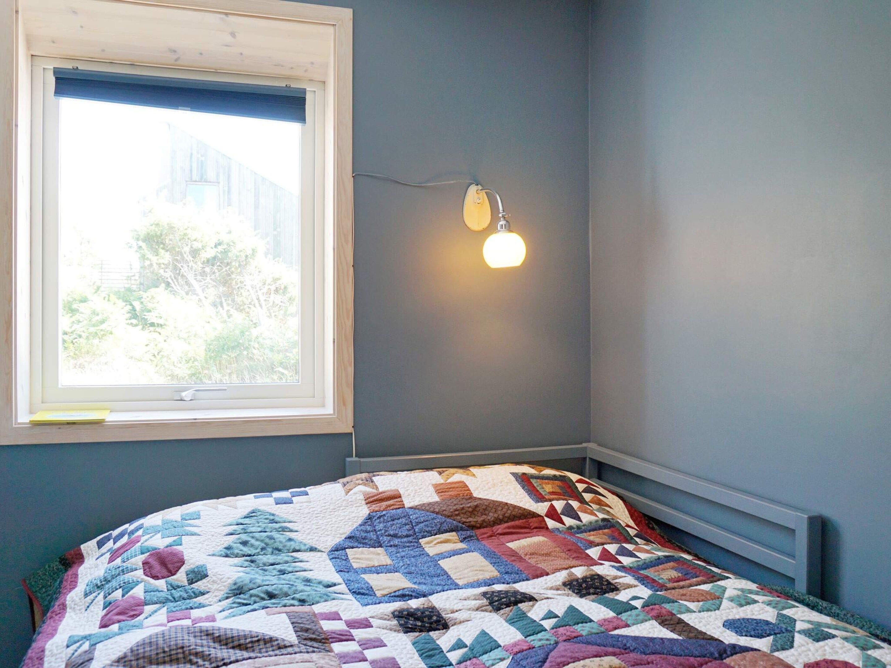 A bedroom with a bed, a window, and a wall-mounted light fixture.