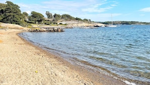 A beach with a rocky shoreline, a pier extending into the water, and a distant view of a hill with trees. - 4 Star Holiday Home in Stromstad (Stromstad)