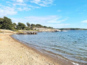 Una spiaggia con un litorale roccioso, un molo che si protende nell'acqua e una vista lontana di una collina alberata.