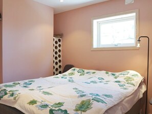 A bedroom with a bed, a window, and a wall-mounted light fixture.