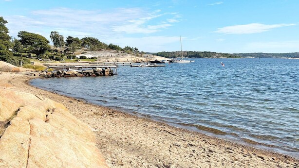 Paisagem costeira com um litoral rochoso, um pequeno cais e barcos na água.