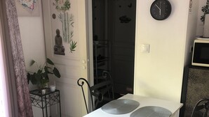 A dining area with a white table, black chairs, and a small side table with a plant.
