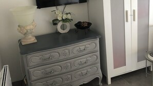 A room with a white cabinet with frosted glass doors, a flat-screen TV mounted on the wall, a decorative vase with flowers, and a small table with a bowl.