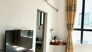 A room with a flat-screen TV on a wooden stand, a window with a curtain, and a small shelf with toiletries. - Tinghai Yushu Hotel (Taishan)