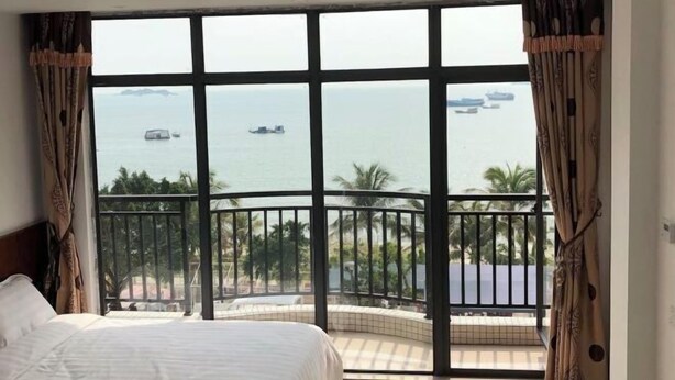 A hotel room with a large window, a bed, and a balcony overlooking the sea. - Tinghai Yushu Hotel (Taishan)