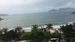 A coastal view with a beach, palm trees, and a distant mountain range. - Tinghai Yushu Hotel (Taishan)