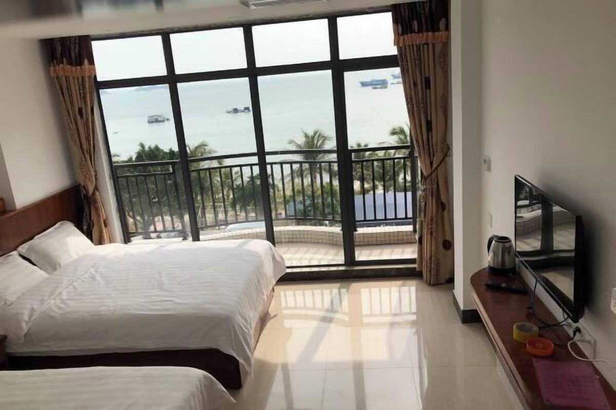 A hotel room with a balcony, a bed, a TV, and a view of the sea.