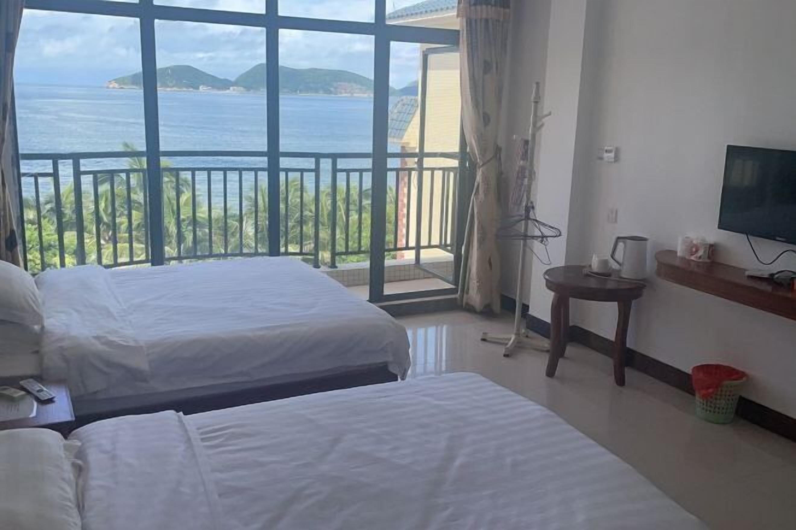 A hotel room with two beds, a TV, a small table, and a view of the sea.