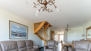 A spacious living room with a large sofa, two armchairs, a wooden staircase, and a dining area. - Bright Coastal Stay in Bredene (Bredene)