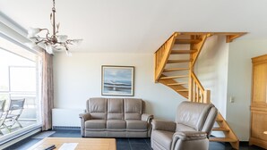 A living room with a sofa, a recliner, a wooden coffee table, a chandelier, a staircase, and a framed picture on the wall. - Bright Coastal Stay in Bredene (Bredene)