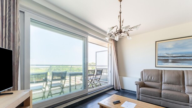 A modern living room with a large window, a sofa, a coffee table, and a TV. - Bright Coastal Stay in Bredene (Bredene)