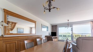 A dining area with a wooden table and chairs, a television, and a balcony with a view. - Bright Coastal Stay in Bredene (Bredene)