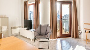 A hotel room with a sofa, a TV, a dining table, and a balcony with curtains. - Apartment in Koksijde Near the Sea (Koksijde)
