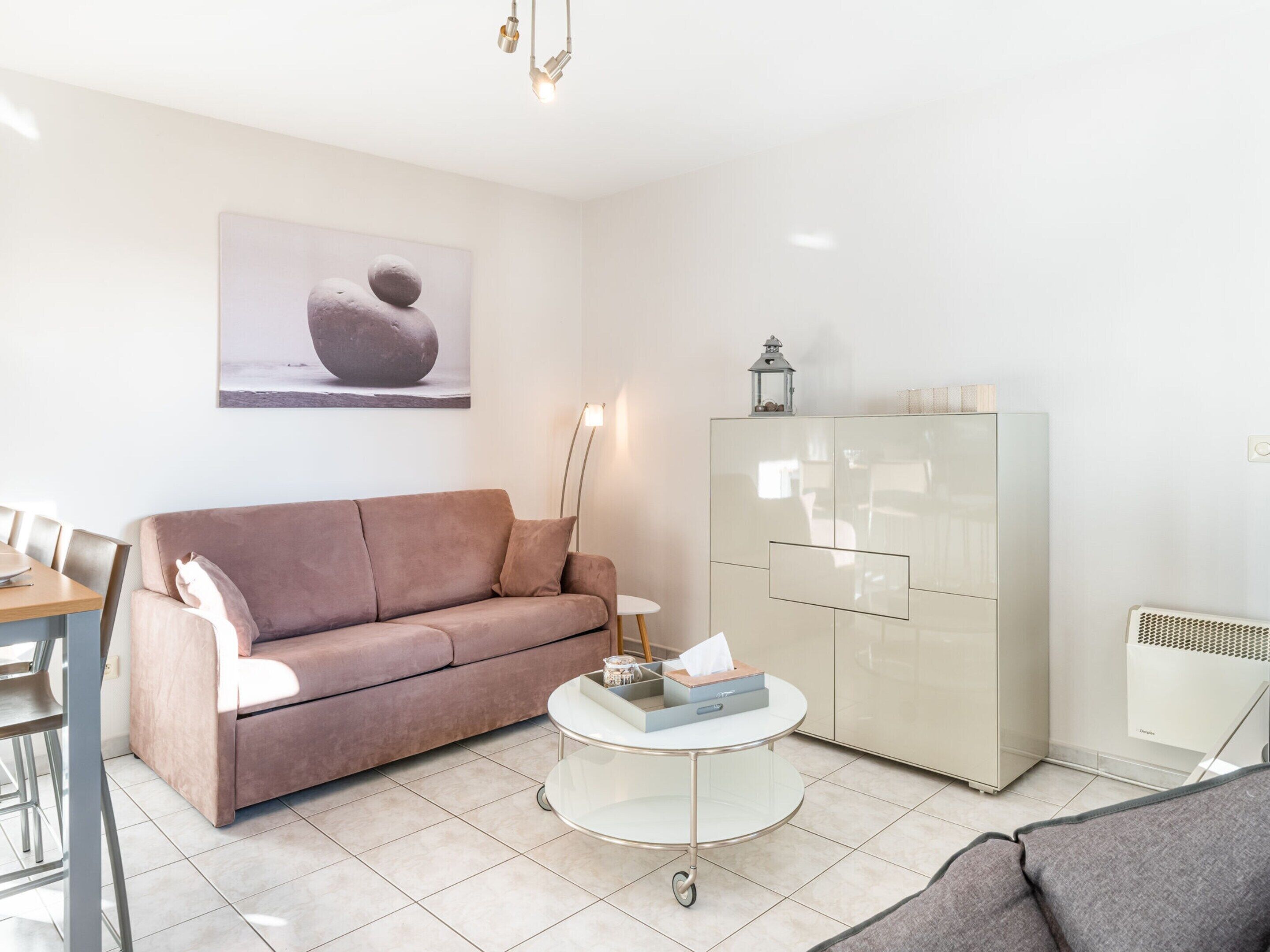 Una sala moderna con un sofá beige, una mesa de centro de vidrio y un mueble blanco.