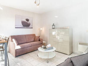 A modern living room with a beige sofa, a glass coffee table, and a white cabinet. - Apartment in Koksijde Near the Sea (Koksijde)