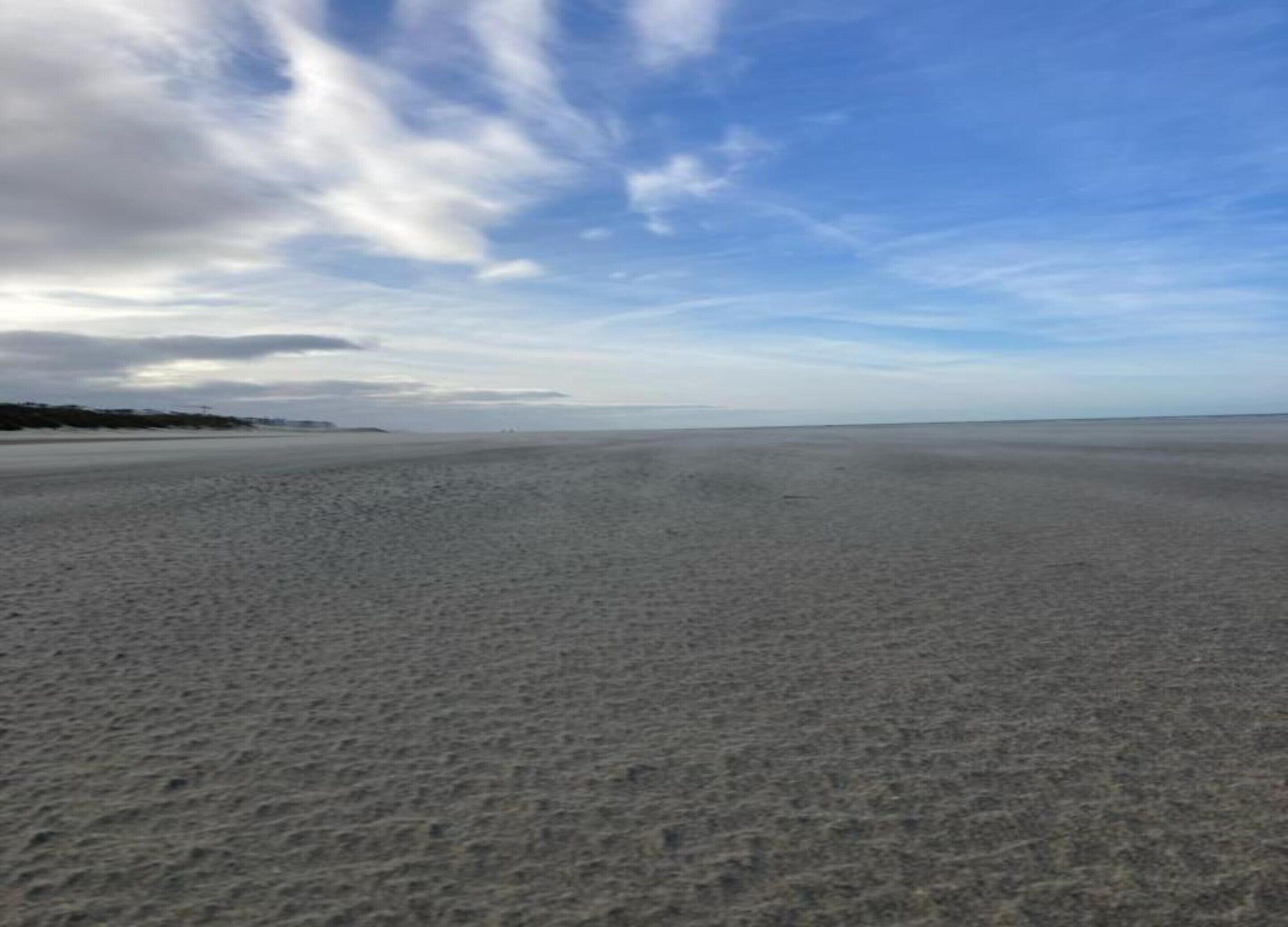 A wide sandy beach with a clear sky and distant land.