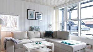 Un salon moderne avec un canapé d’angle, une table basse blanche et une grande fenêtre donnant sur la rue.