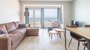 A modern living room with a brown leather sofa, a wooden dining table with chairs, and a television. - Apartment on the 5th Floor With sea View (Middelkerke)