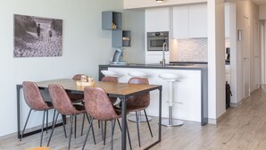 A modern kitchen with a central island, bar stools, and a dining table with chairs. - Apartment on the 5th Floor With sea View (Middelkerke)